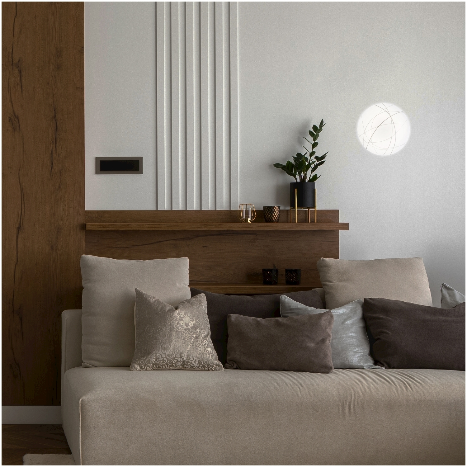 Divano beige con cuscini, contro un pannello di legno e una parete bianca con luce decorativa.