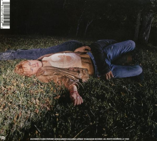Zwei Personen auf Gras, eine liegt. Braune Jacke, Jeans und dunkler Hintergrund mit Baum.