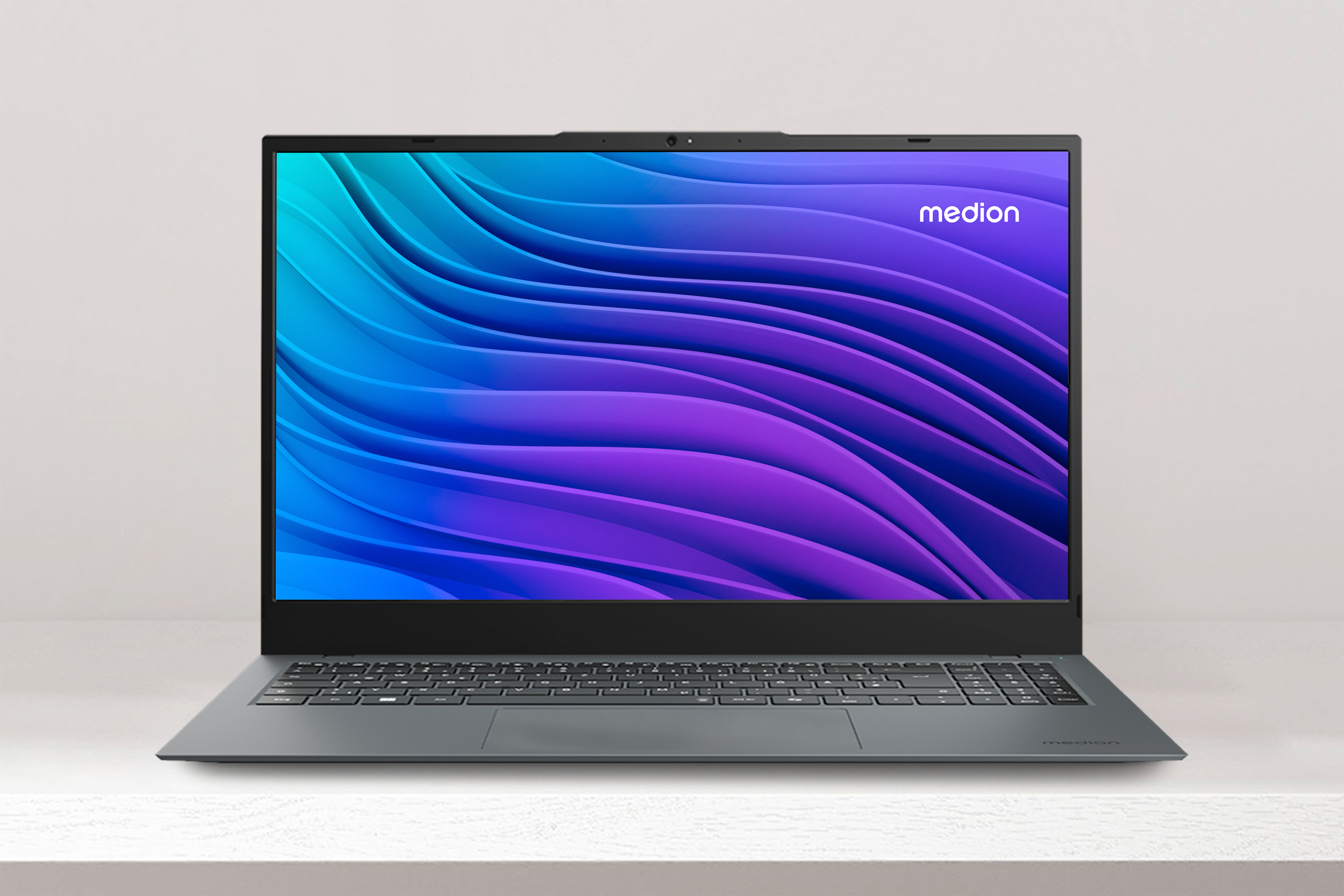 Offener grauer Laptop mit blau-lila Farbverlauf auf weißem Schreibtisch.