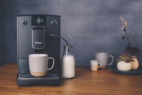 Czarny ekspres do kawy z kubkiem i butelką mleka na stole.