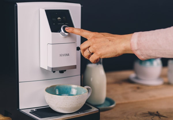 Ręka naciska przycisk na czarno-białym ekspresie do kawy.