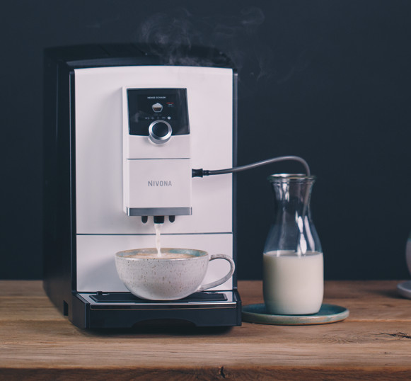 Ekspres do kawy wlewa mleko do filiżanki kawy. Szklany pojemnik na mleko. Ciemne tło.