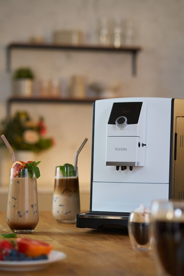 Ekspres do kawy z dwoma napojami mrożonymi i talerzem owoców na drewnianym stole.