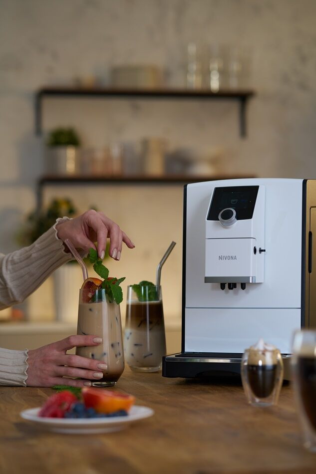 Osoba dodaje miętę do koktajlu. Ekspres do kawy i szklanki na drewnianym blacie.