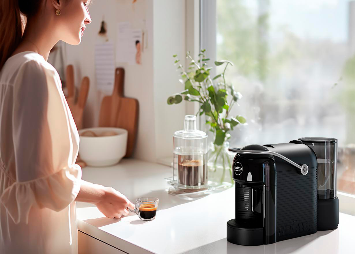Frau macht Kaffee. Schwarze Kaffeemaschine, eine Tasse Kaffee und ein Fenster.