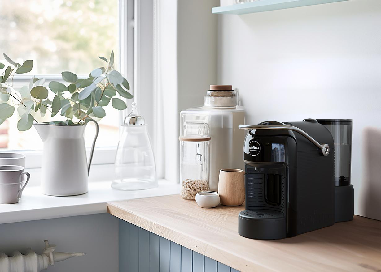 Küchentheke mit Kaffeemaschine, Vase mit Blättern, Gläsern und einem Fenster.