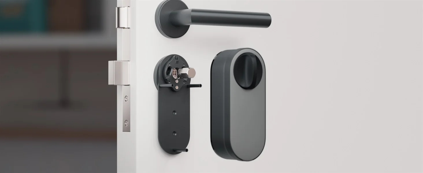 Elementy inteligentnego zamka zamontowane na białych drzwiach, widoczna klamka i cylinder.