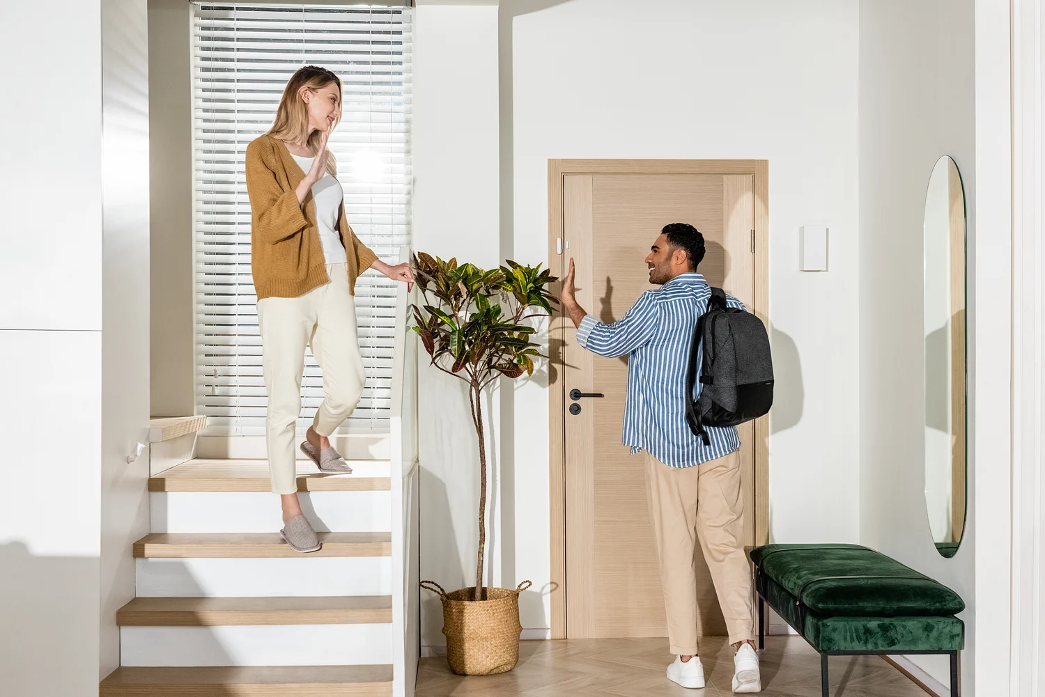 Kobieta w brązowym swetrze na schodach, mężczyzna przy drzwiach z plecakiem.