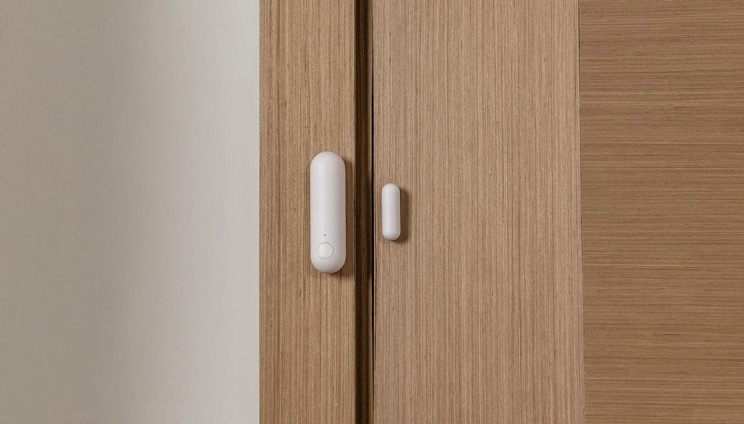 Biały czujnik inteligentnego domu zainstalowany na drewnianej ramie drzwi, widoczne dwie części.