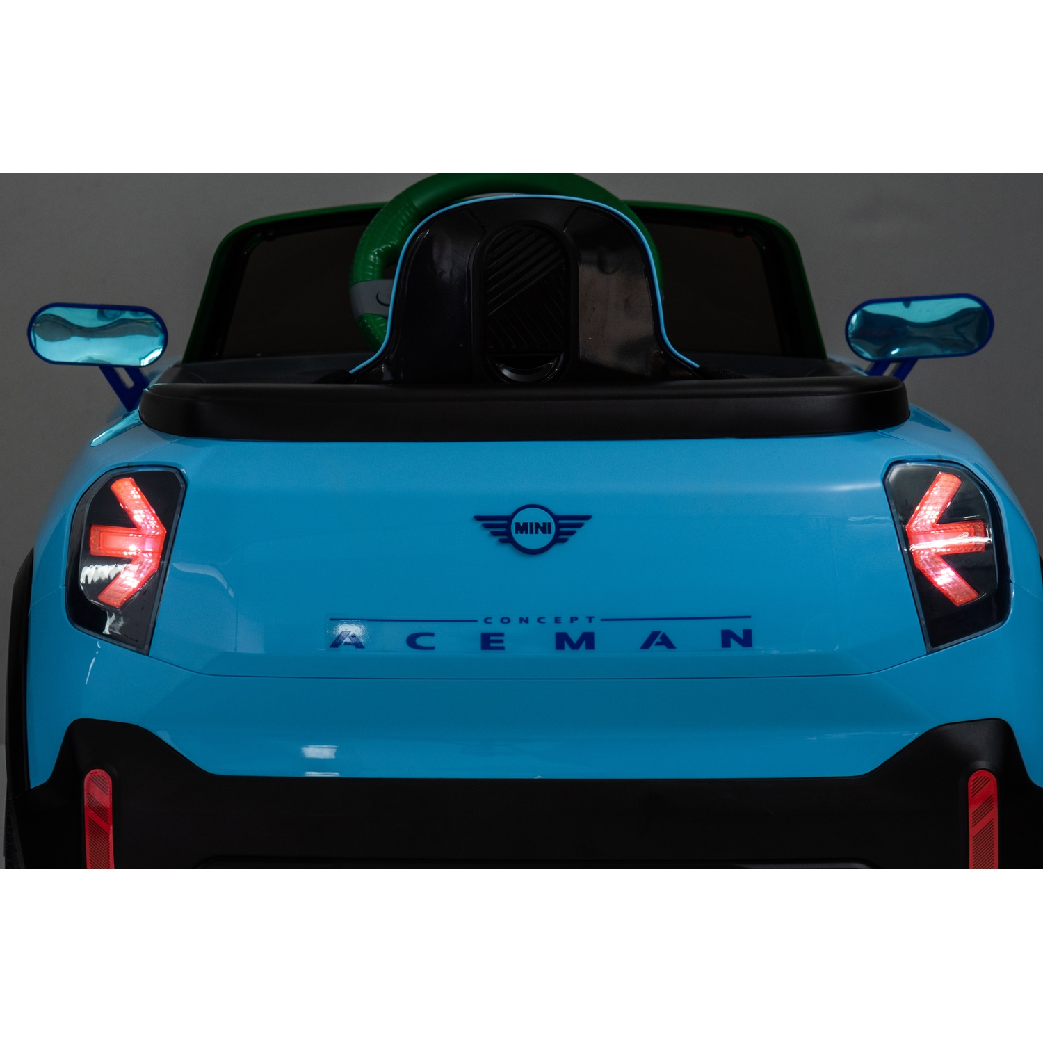 Rear view of a blue Mini electric car toy. Features lights, logo, and a green steering wheel.