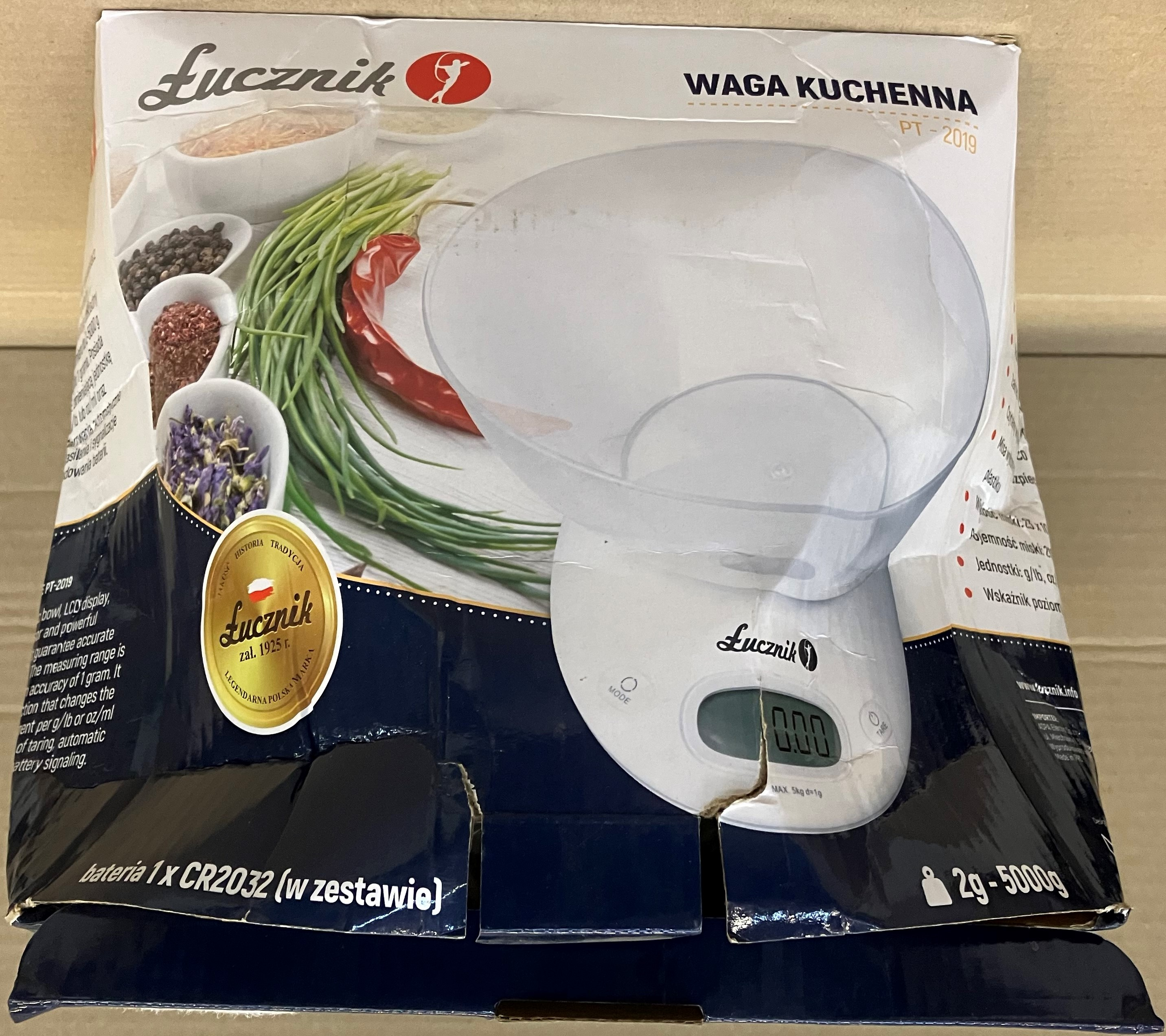 Biała waga kuchenna z przezroczystą miską, na kartonie.