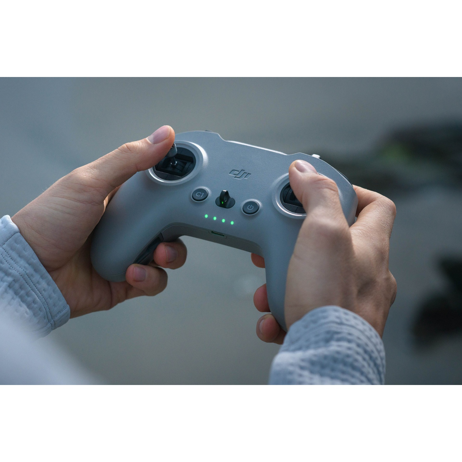 Mani che tengono un controller grigio con pulsanti e luci contro uno sfondo sfocato.