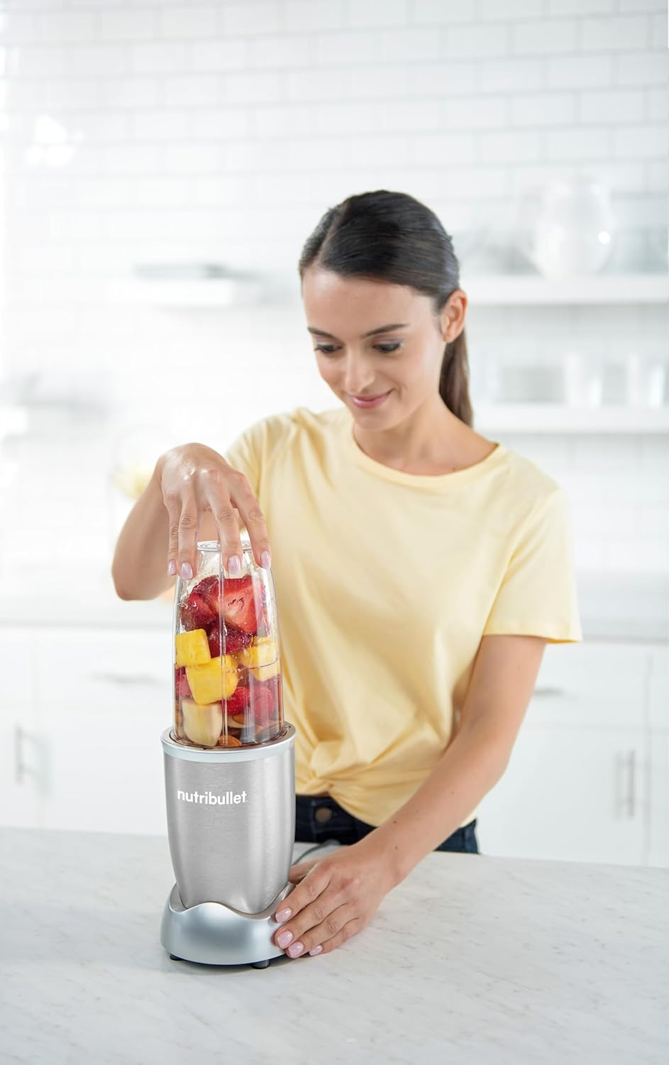Una donna usa un frullatore per fare un frullato con frutta. Il frullatore è su un bancone.