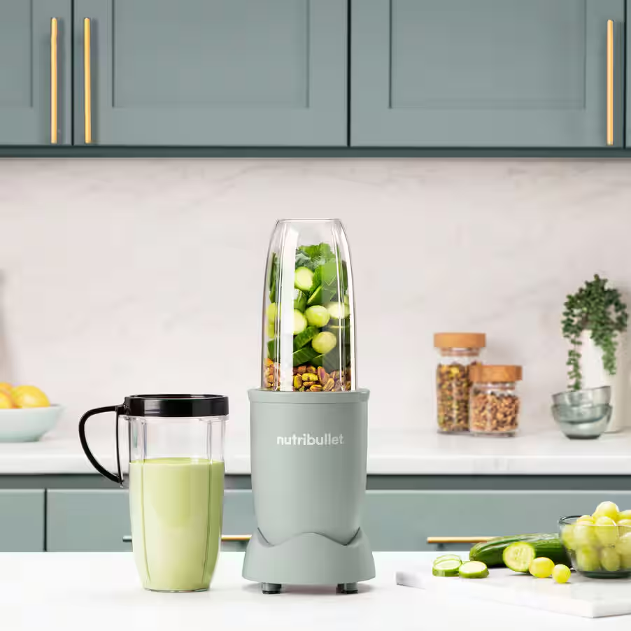 Ein Mixer mit grünem Inhalt, ein Glas mit grüner Flüssigkeit und Zutaten.