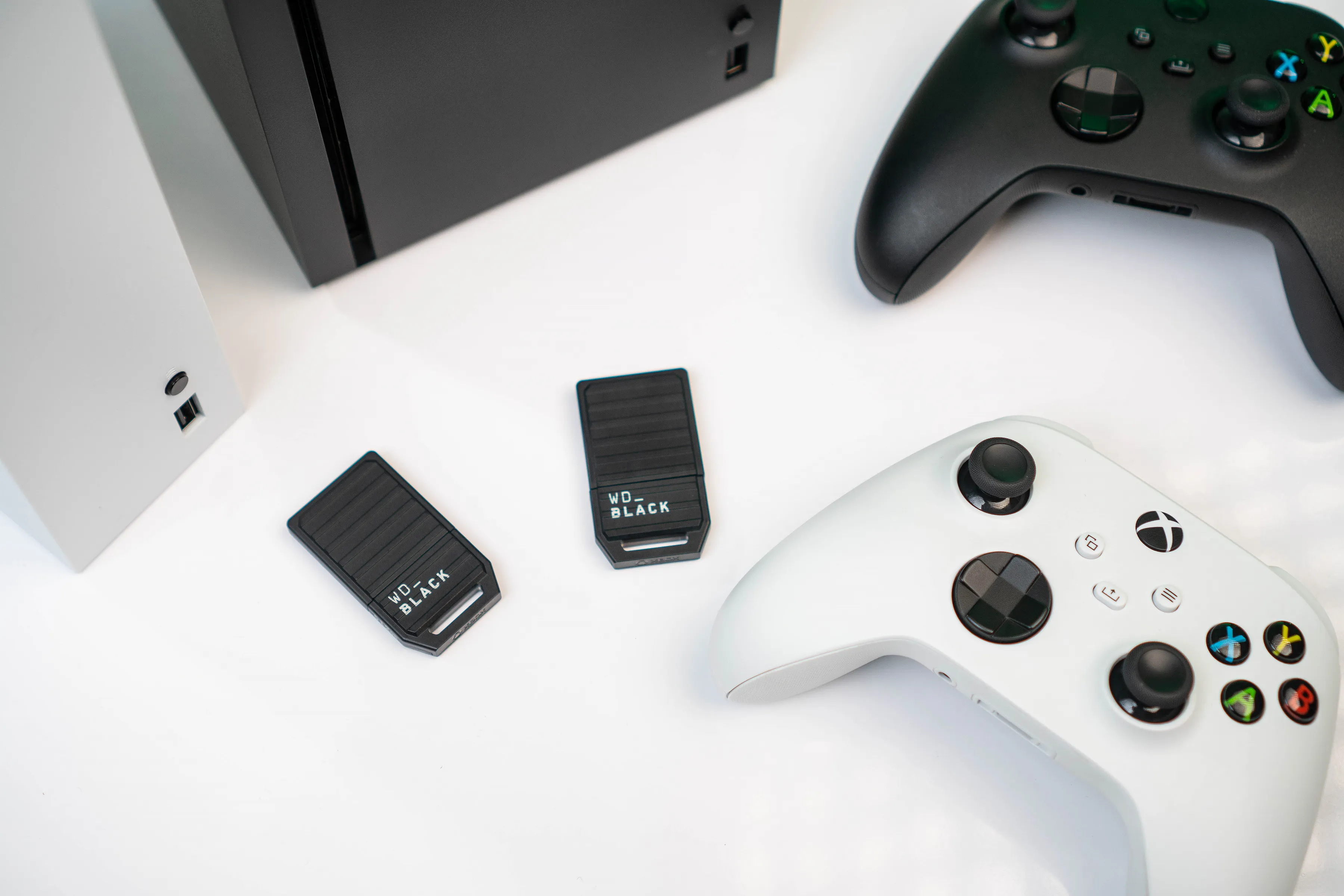 Drei WD_BLACK externe Festplatten und zwei Xbox-Controller auf weißer Oberfläche.