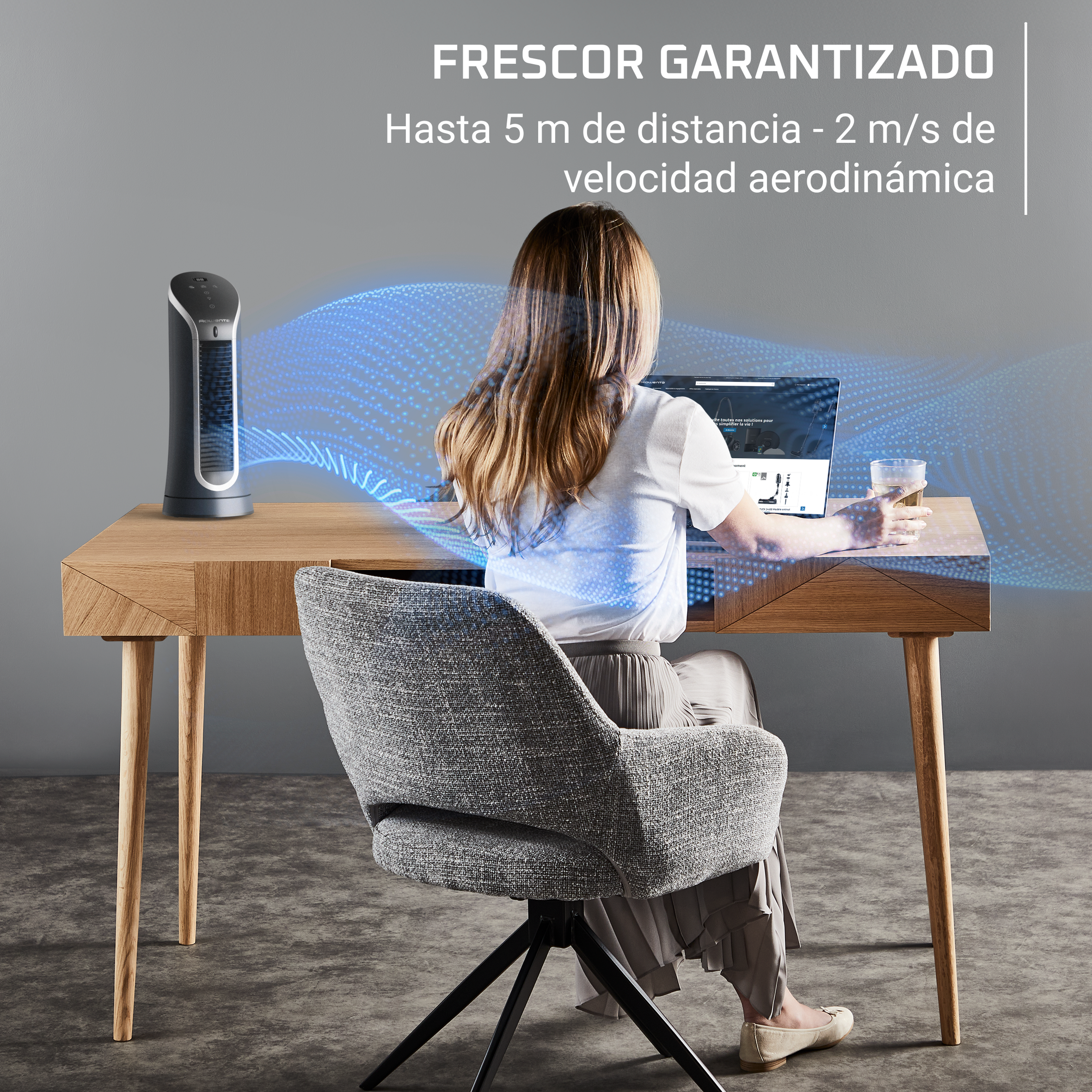 Mujer trabajando en un portátil, con un ventilador, en un escritorio de madera.