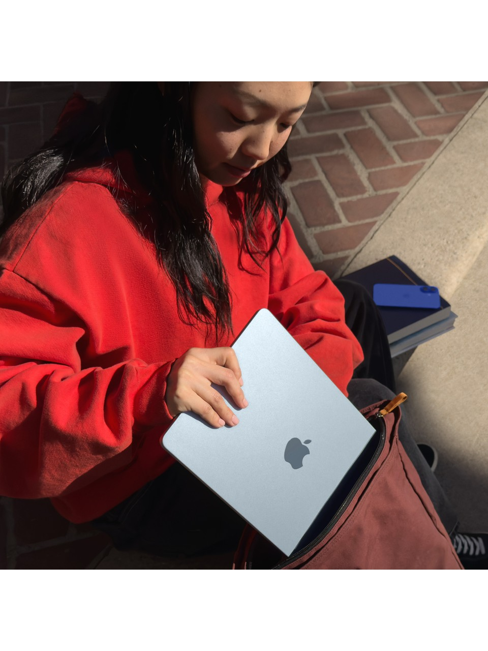 Kırmızı kapüşonlu bir kişi, üzerinde Apple logosu bulunan açık mavi bir dizüstü bilgisayarı açıyor.