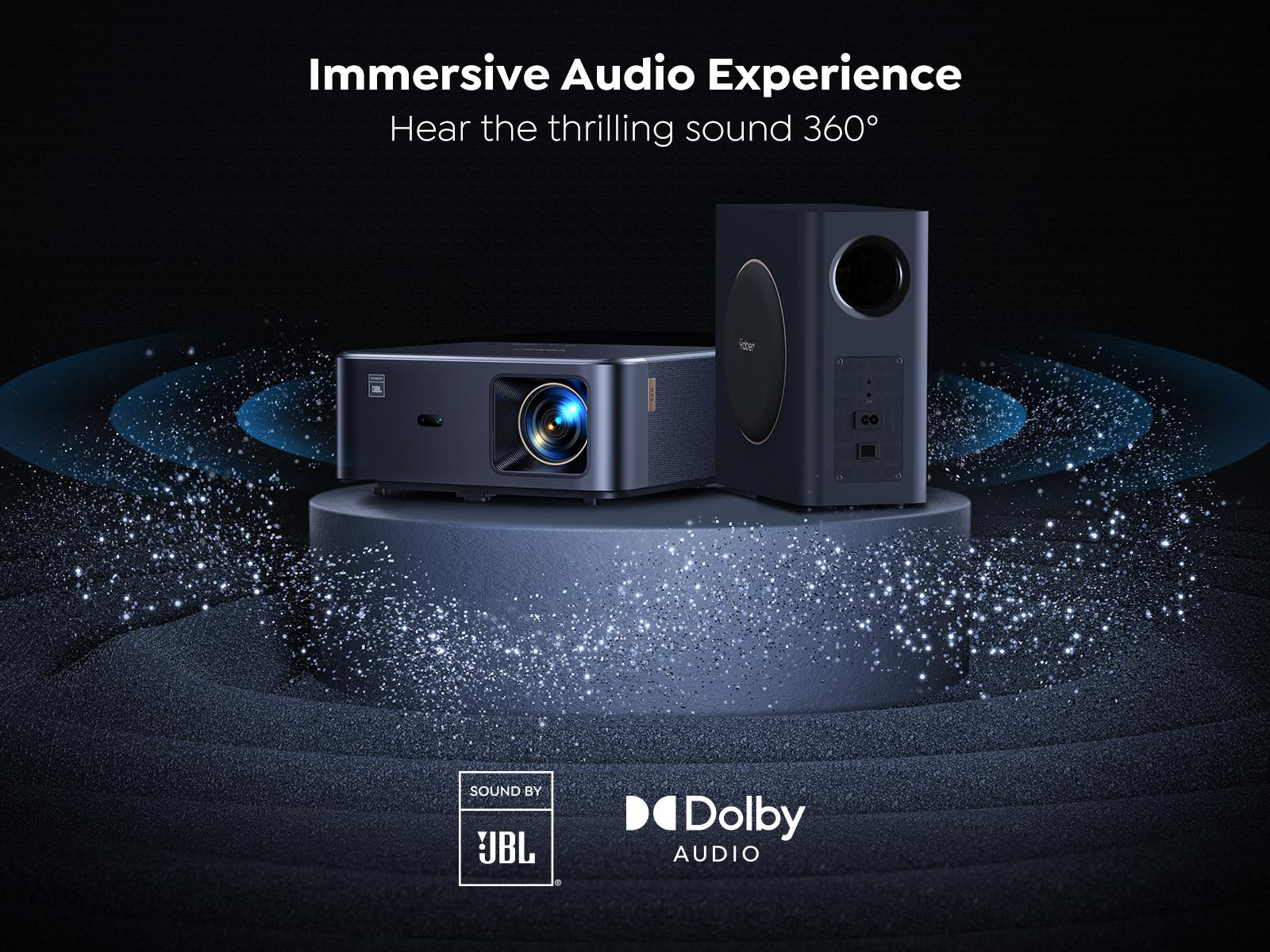 Ein schwarzer Projektor und Subwoofer auf einer dunklen Plattform, umgeben von blauen Partikeleffekten. Logos von JBL und Dolby.