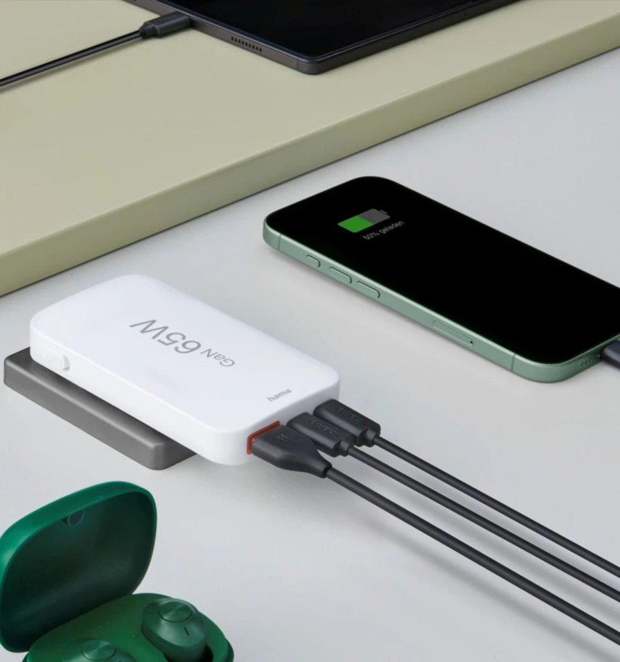 Biały power bank ładujący telefon czarnym kablem i para zielonych słuchawek w etui.