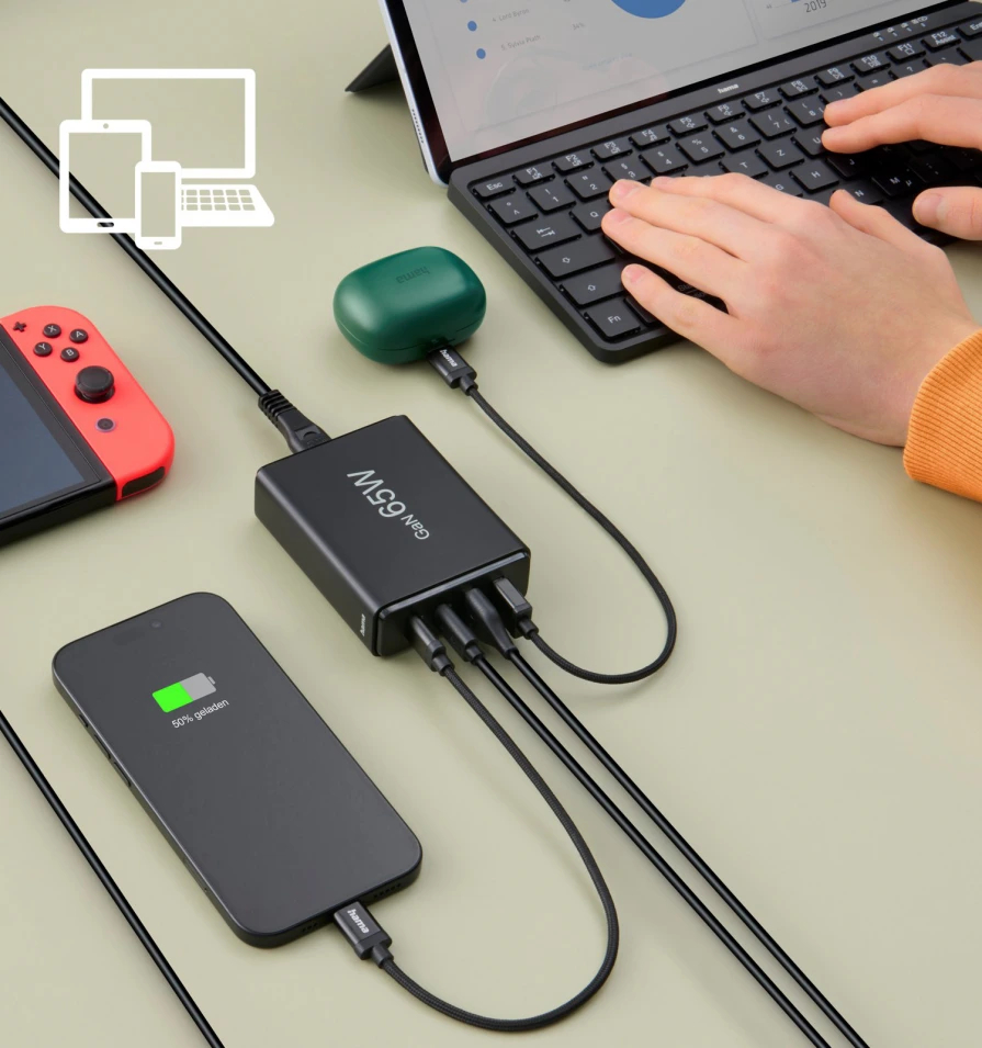 Telefon i inne urządzenia ładujące się z czarnej ładowarki za pomocą kabli.