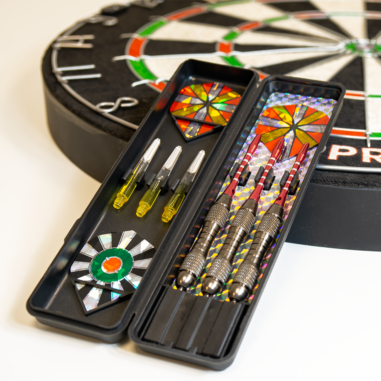 Een dartbord met darts in een etui. De darts zijn rood en zilver. De etui is zwart. De achtergrond is wit.