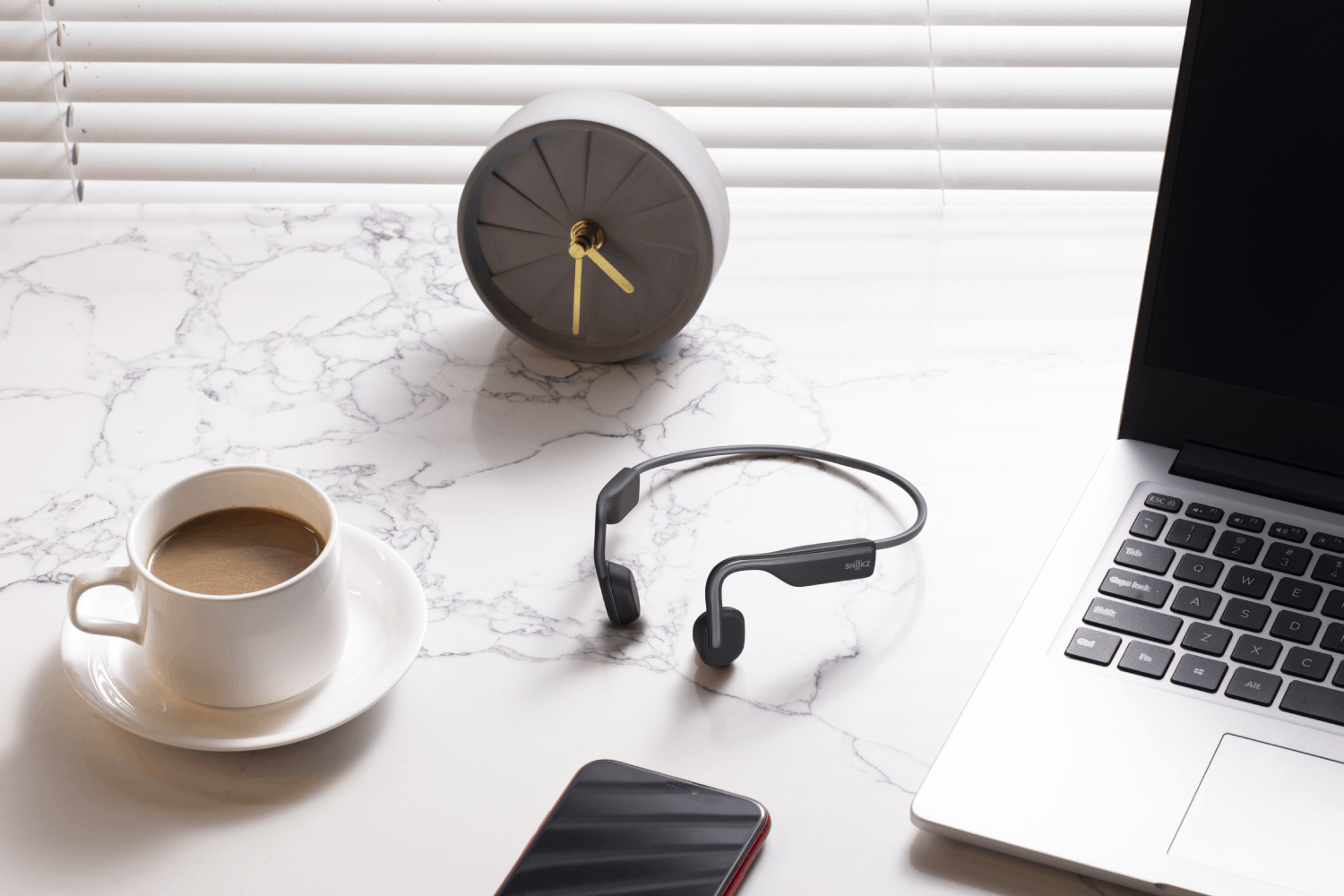 Taza blanca, auriculares y teléfono inteligente en mesa de mármol con reloj.