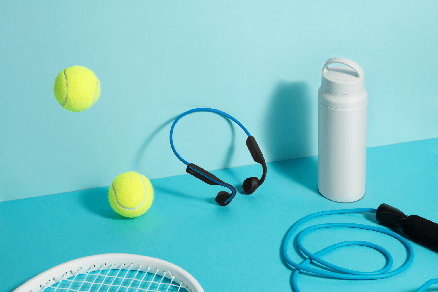 Auriculares azules, pelotas de tenis, botella de agua y cuerda de saltar.