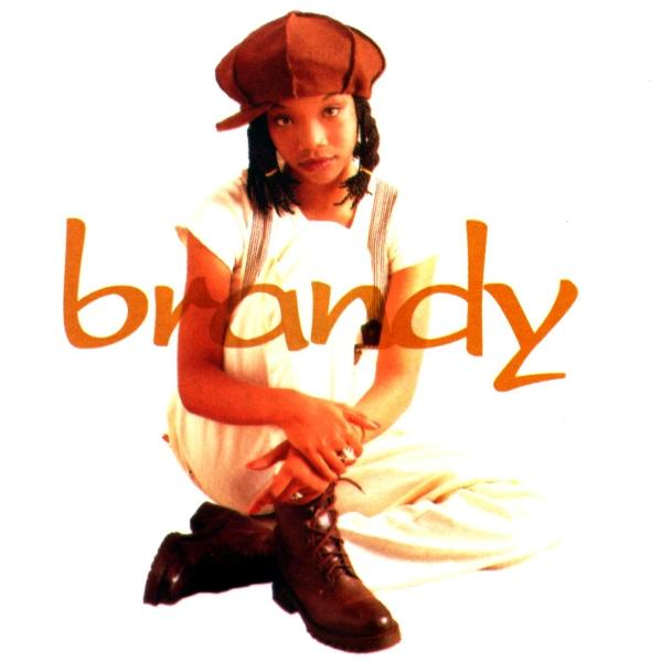Brandy kniet, trägt eine Mütze, ein weißes Oberteil und eine Hose, mit dem Wort "brandy" in Orange.