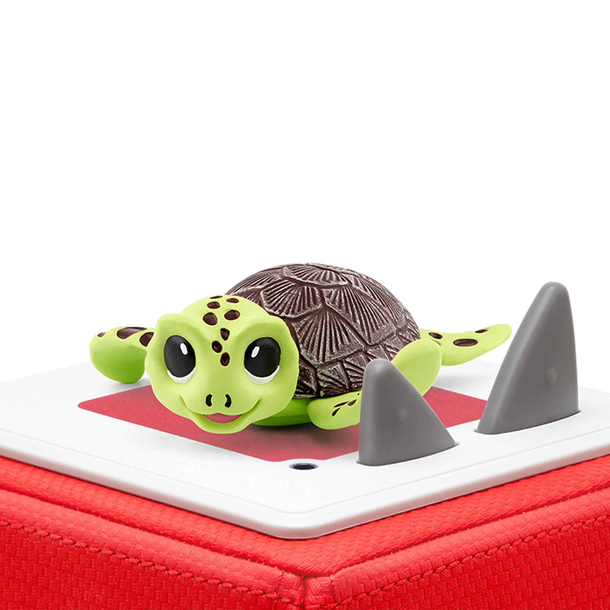 Grünes Schildkrötenspielzeug mit braunem Panzer auf roter und weißer Oberfläche mit grauen Haifischflossen.