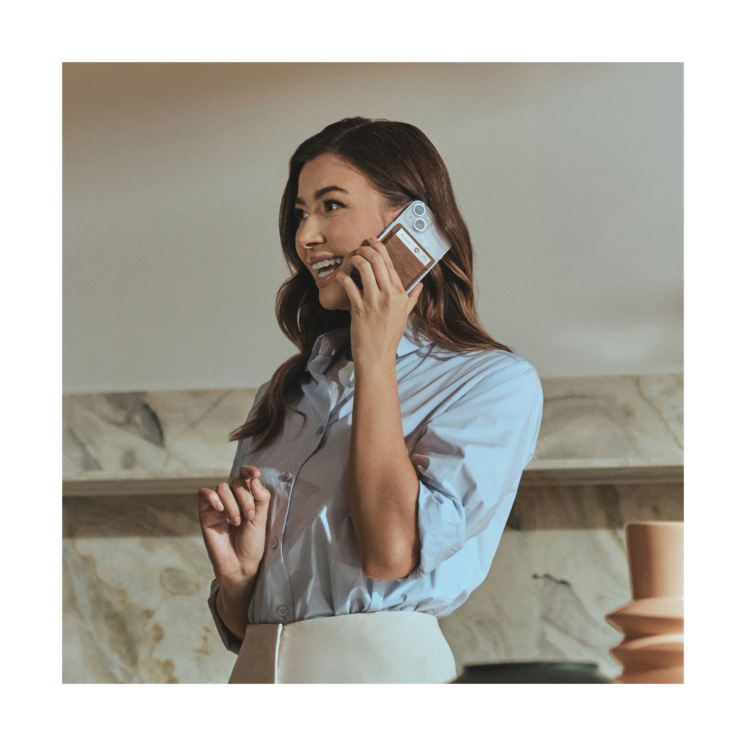 Una donna al telefono sorridente e tiene una custodia, sfondo chiaro.