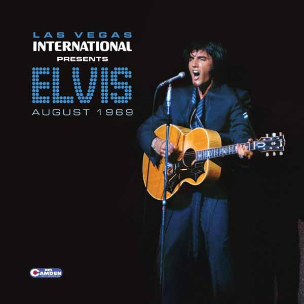 Elvis en costume, guitare, chantant sur scène. Contexte : Las Vegas International, août 1969.
