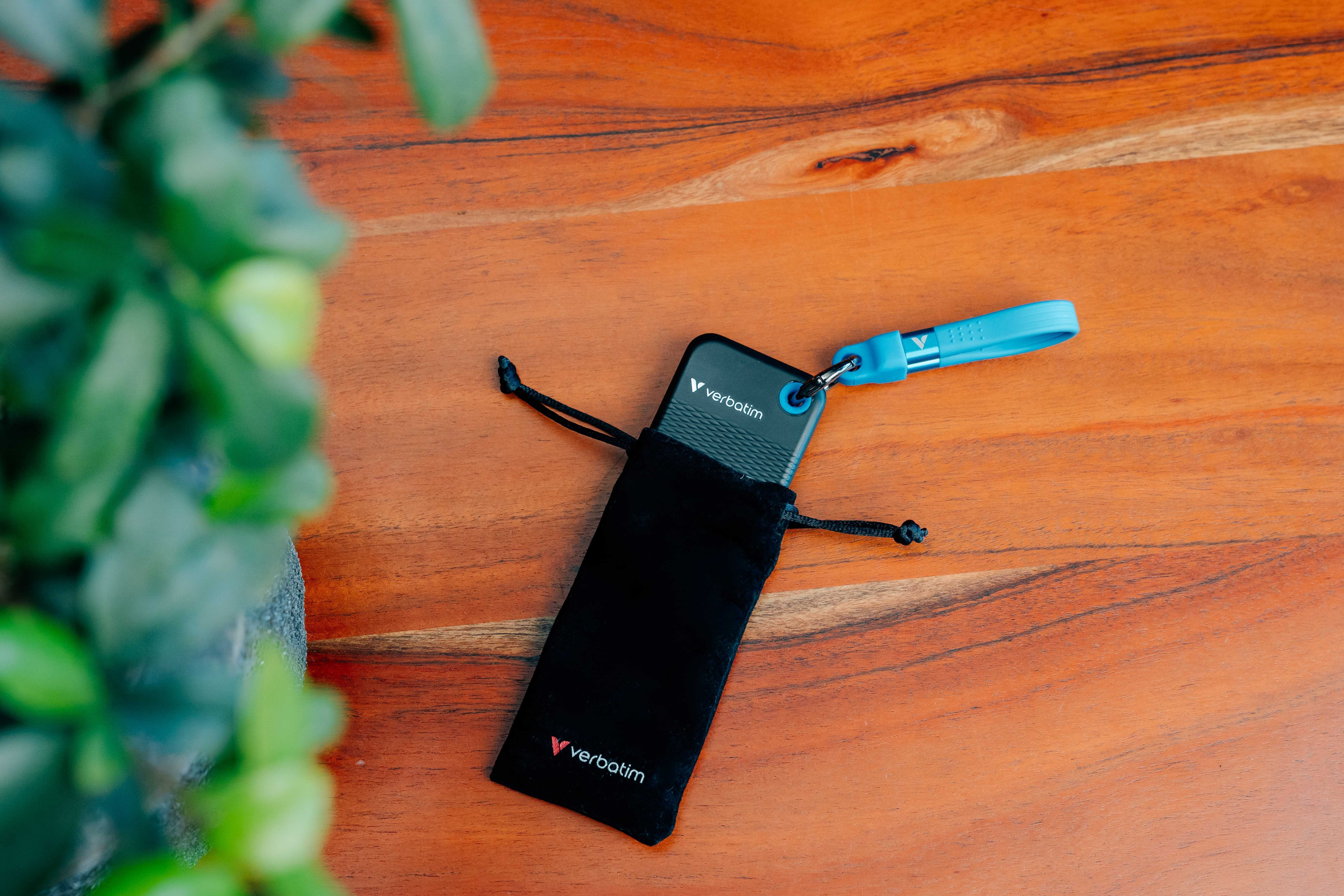 Verbatim USB-Stick in schwarzem Beutel mit blauem Schlüsselband auf Holztisch.