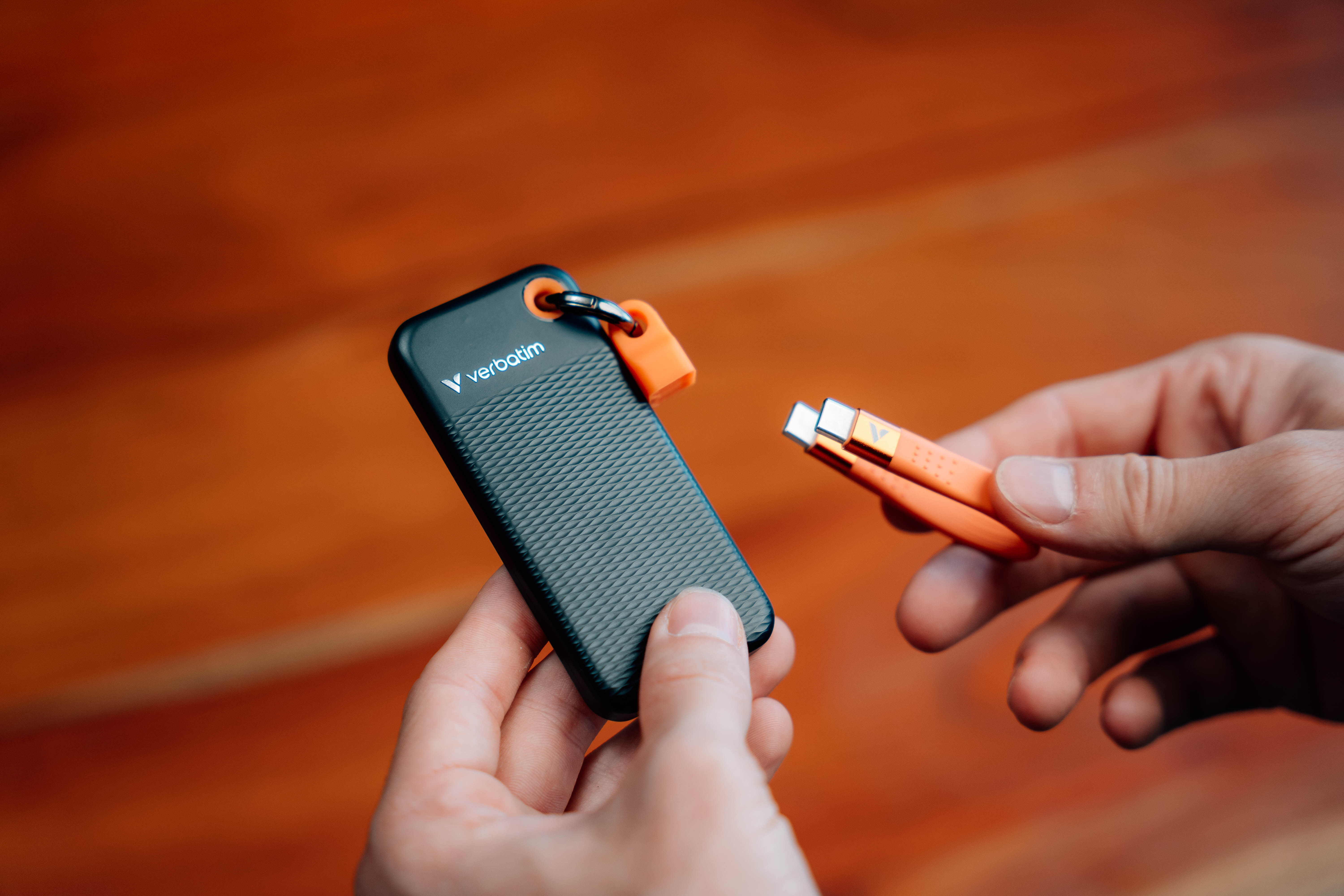 Hände halten schwarzen USB-Stick mit orangefarbenem Clip, neben einem orangefarbenen Adapter.
