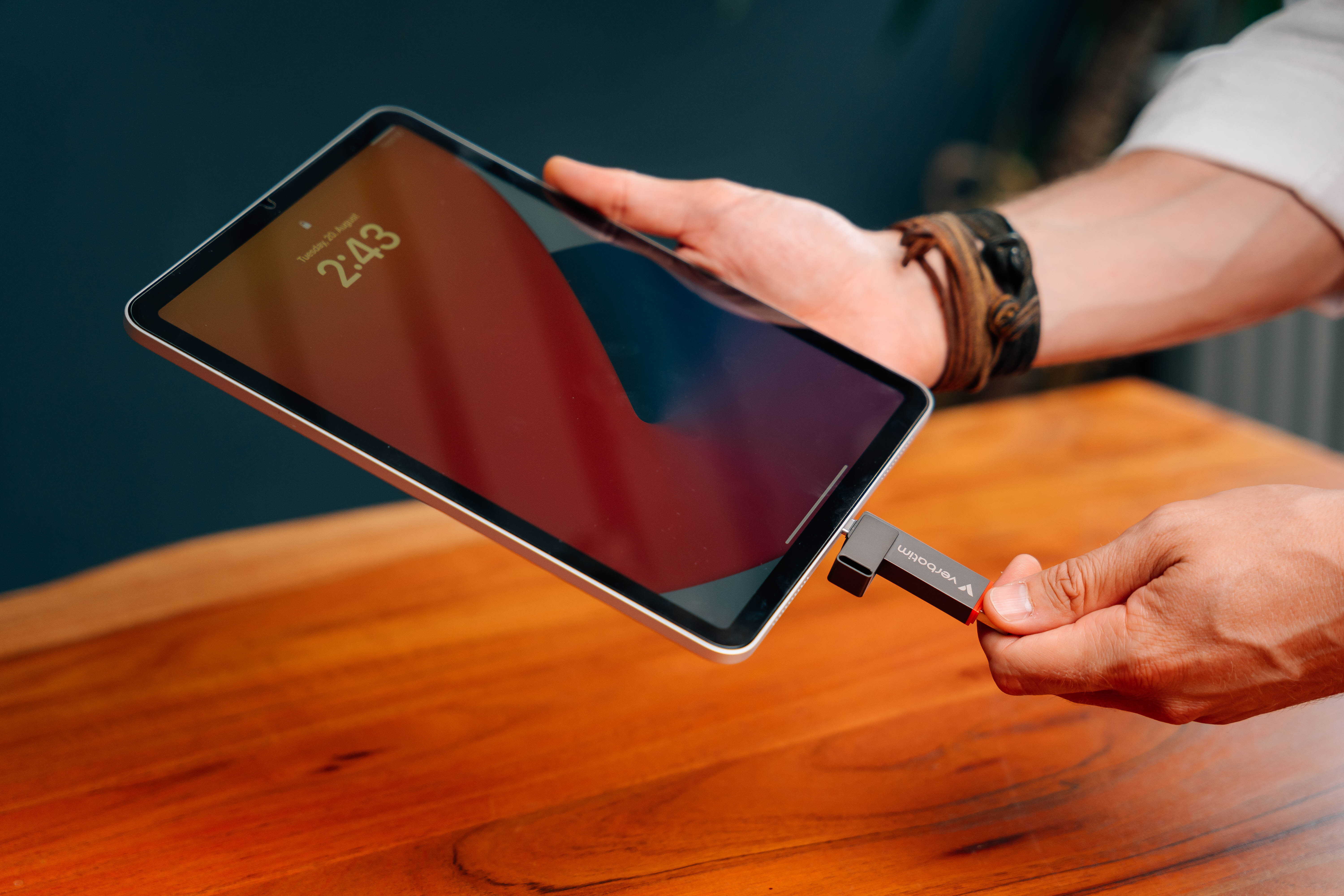 Ein Tablet, verbunden mit einem USB-C-Adapter, gehalten von einer Person auf einem Holztisch, Lederarmband.