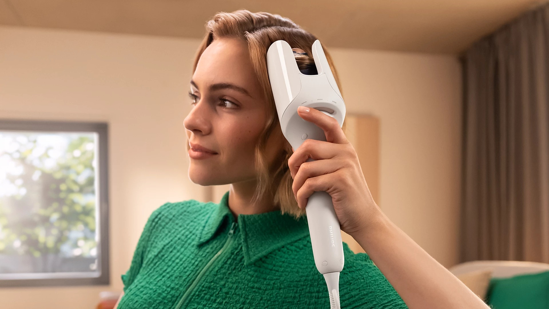 Kobieta używająca białego urządzenia do pielęgnacji włosów, zielona góra, neutralne tło.