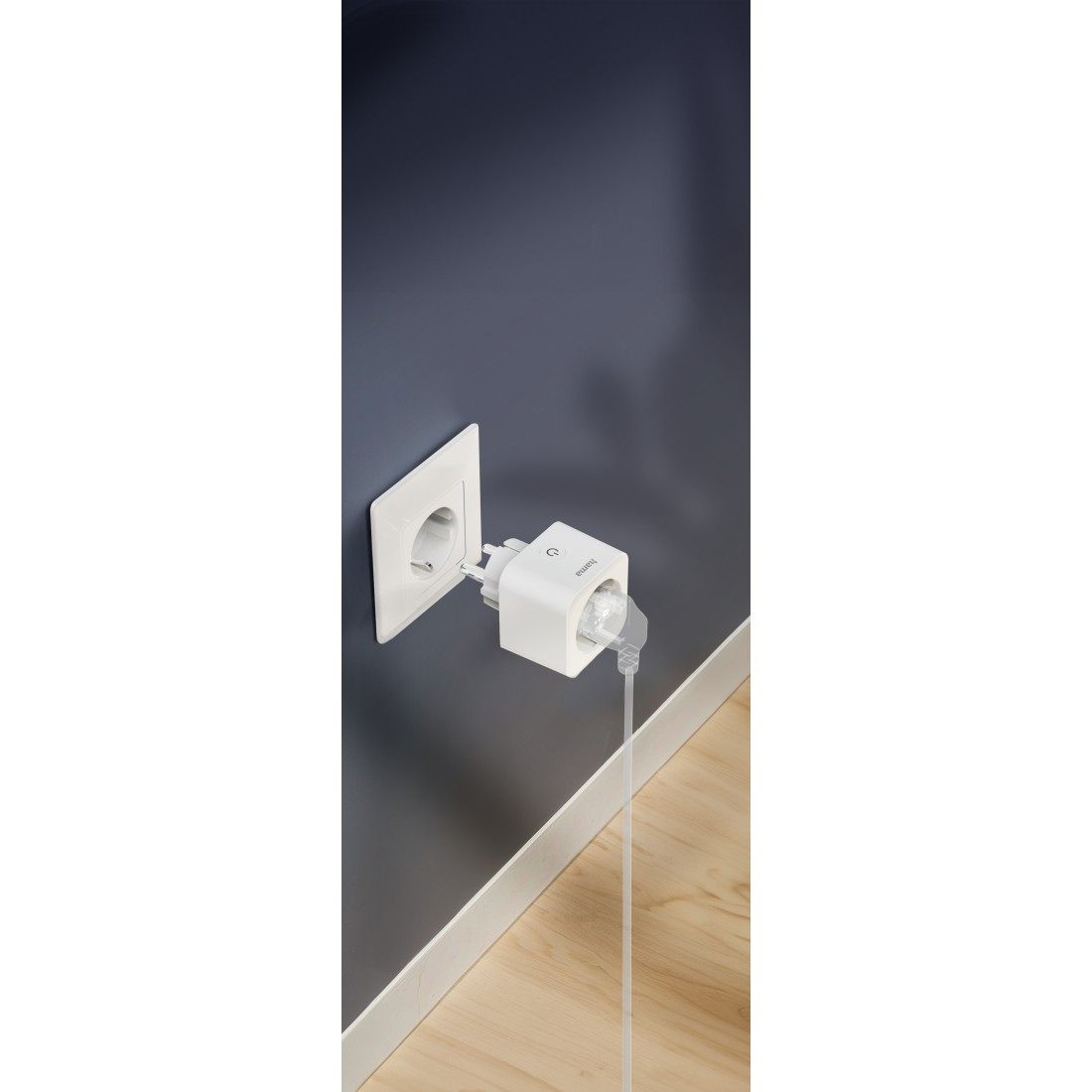 Ein weißer Smart Plug in einer Steckdose, verbunden mit einem Kabel, an einer dunkelblauen Wand.