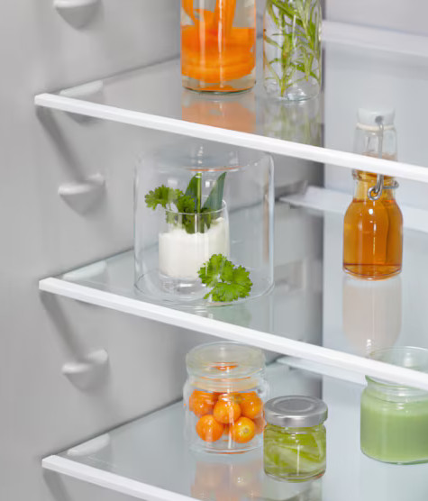 Wnętrze lodówki z półkami, na których znajdują się słoiki z jedzeniem i ziołami w szklanych pojemnikach.