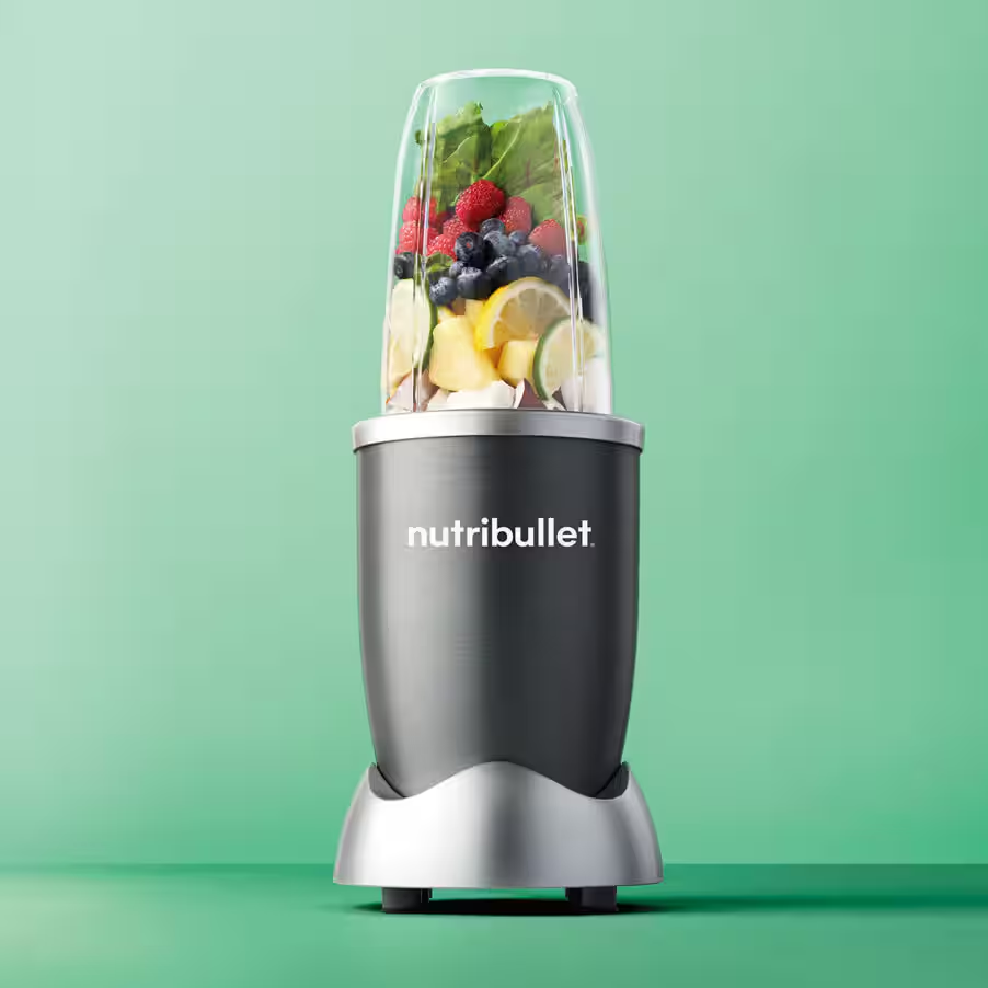 Ein Nutribullet-Mixer, gefüllt mit Früchten und Grünzeug, auf grünem Hintergrund.