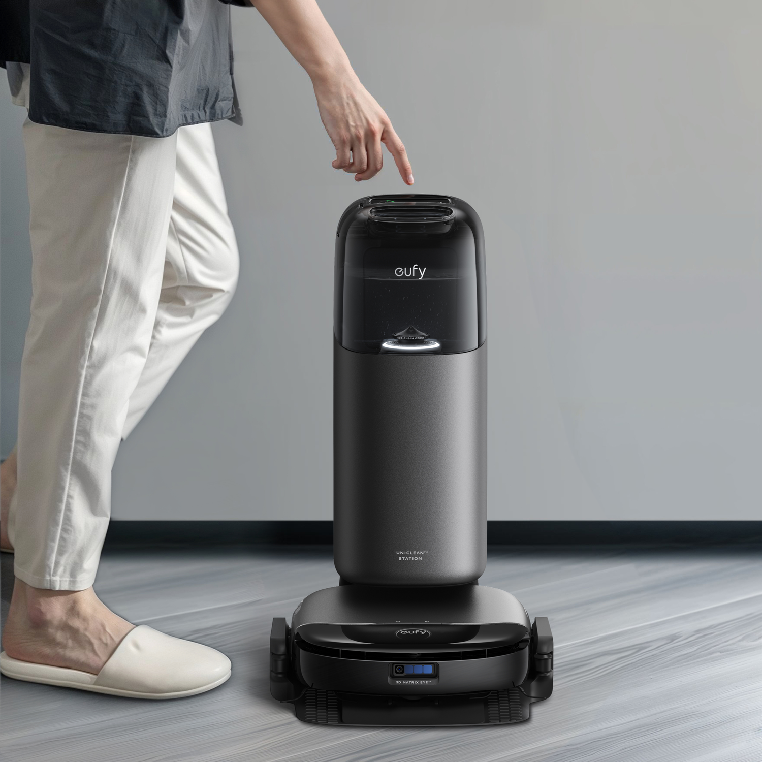 Une main touche un aspirateur robot cylindrique noir avec une station de charge.
