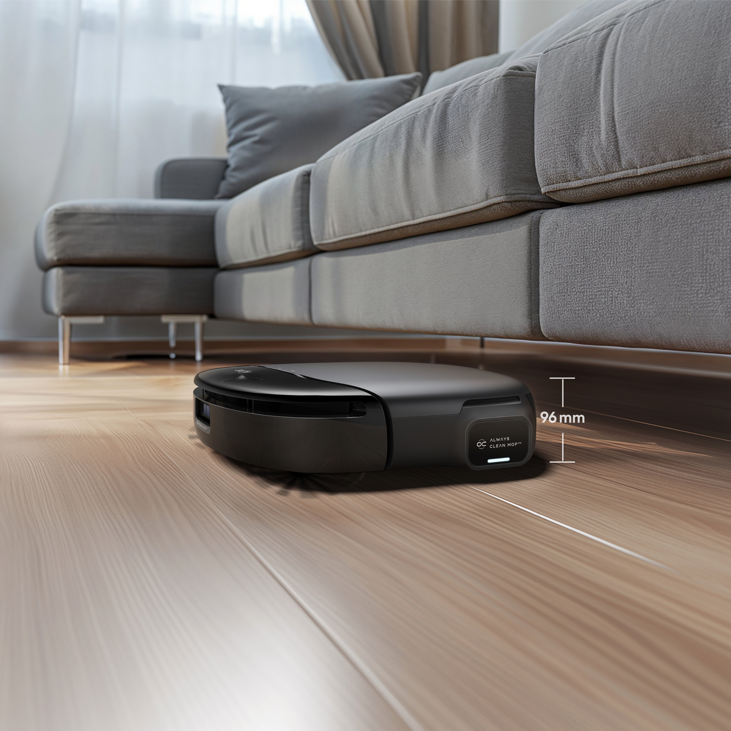 Un aspirateur robot noir nettoie le sol en bois sous un canapé gris.
