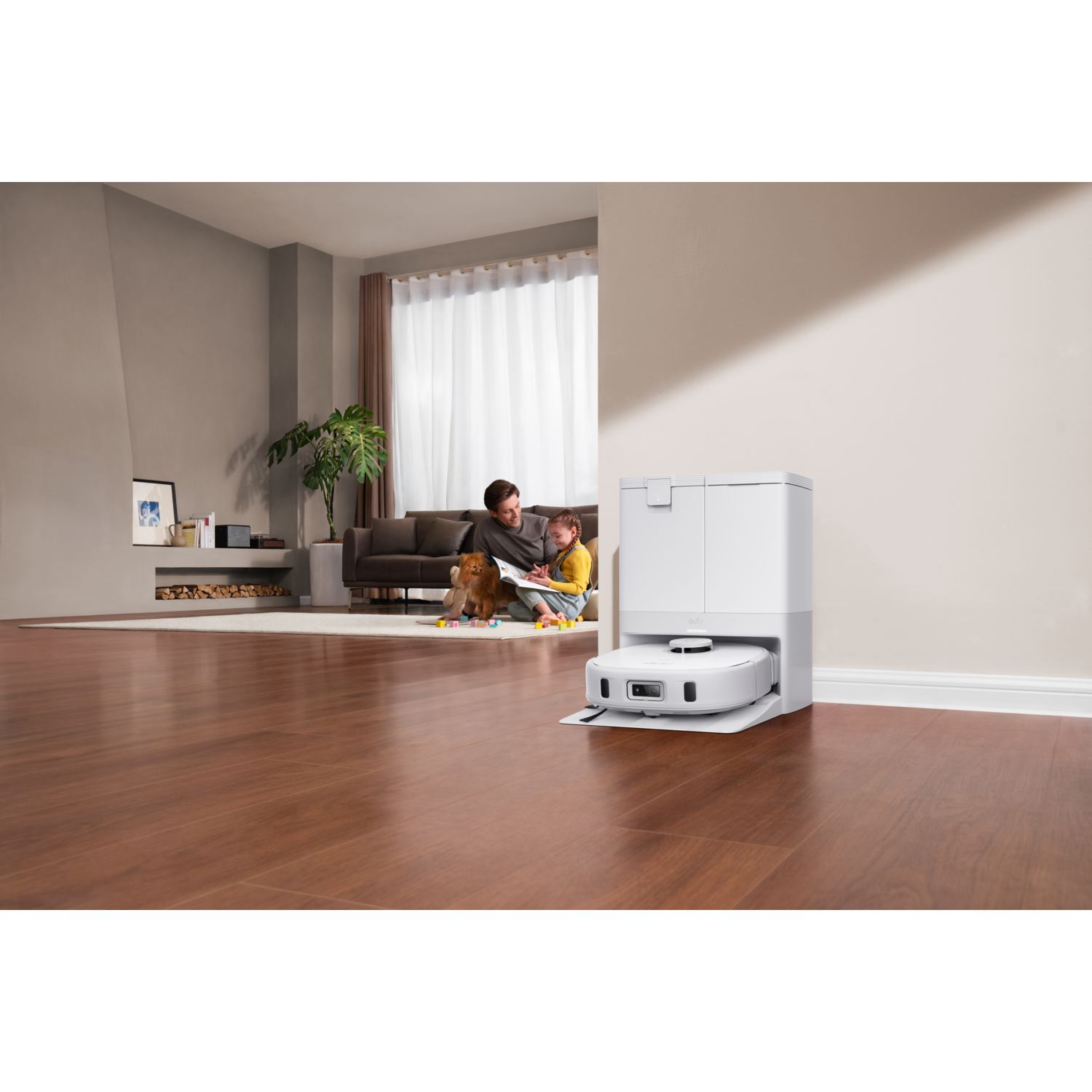 A man and a child sit near a robot vacuum cleaner.