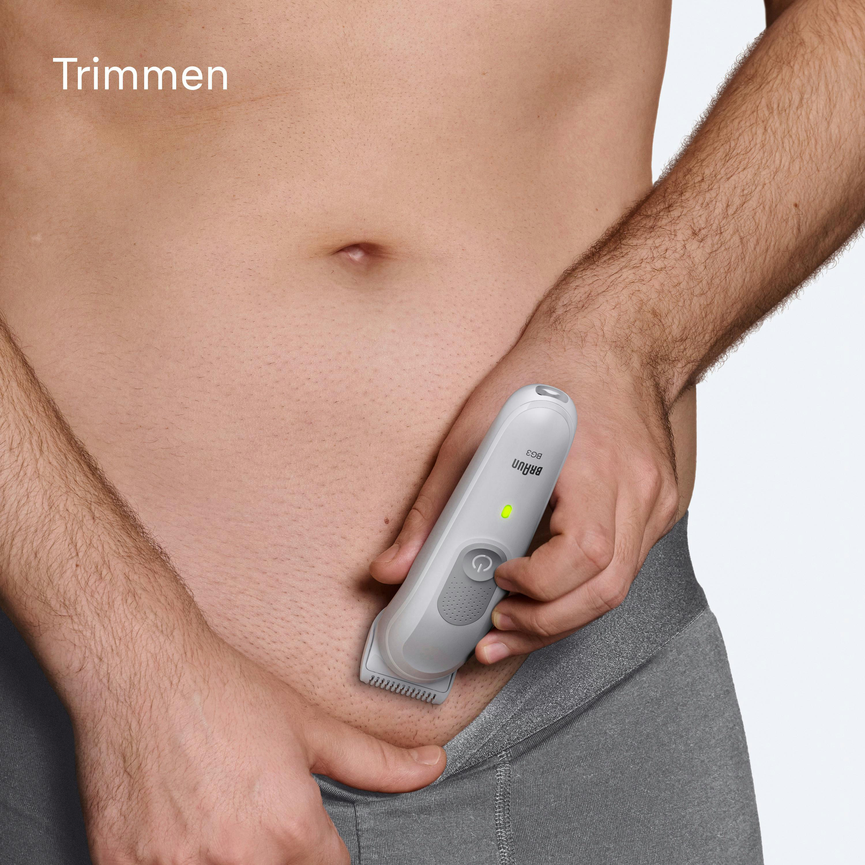 Ein Mann rasiert sein Schamhaar mit einem weiß-grauen Trimmer. Das Wort „Trimmen“ steht oben.