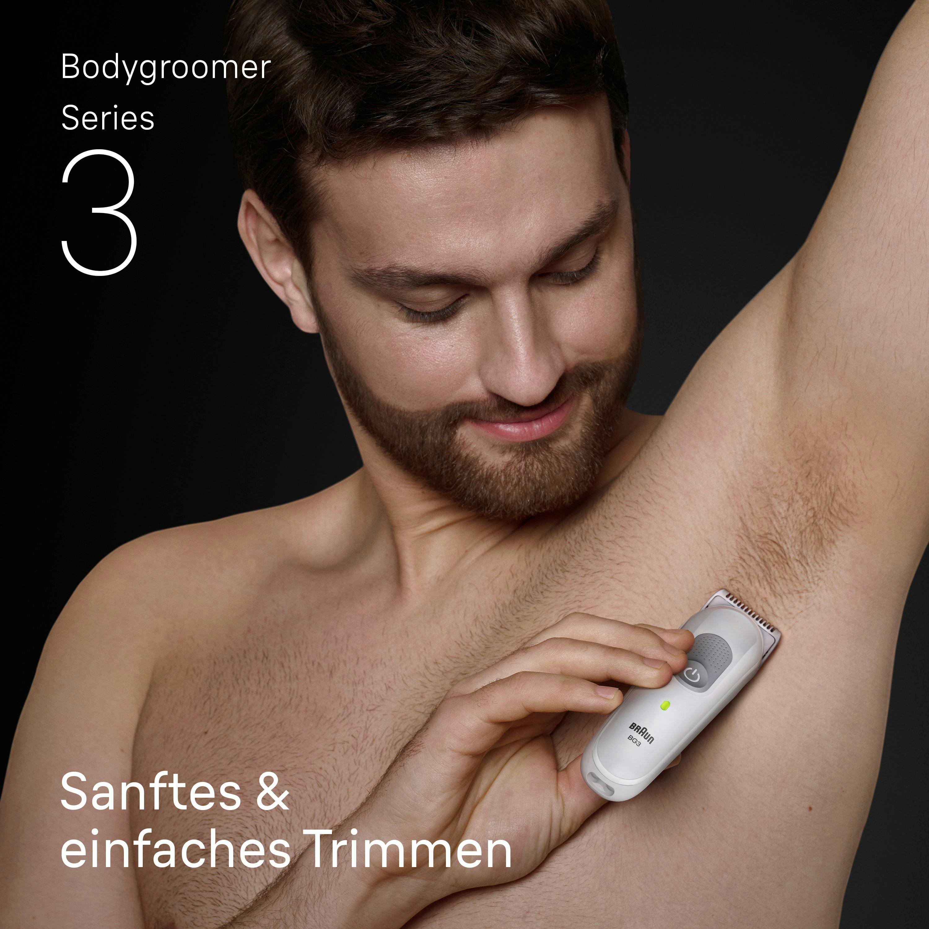 Mann rasiert Achselhaare mit weißem Bodygroomer auf schwarzem Grund.