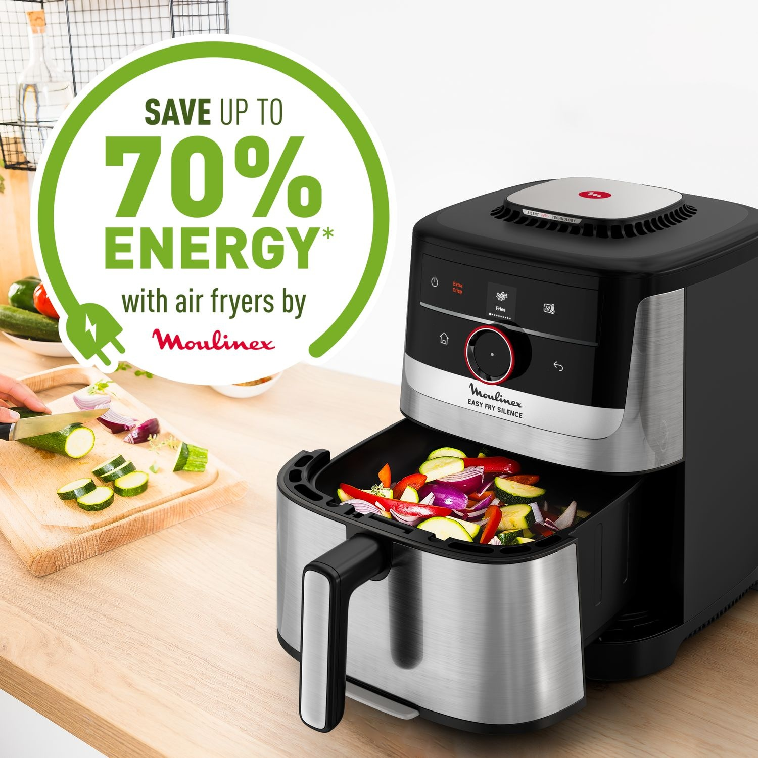 Un airfryer avec une façade noire et des côtés argentés. Des légumes sont dans le panier. Le texte dit 'Save up to 70% Energy'.
