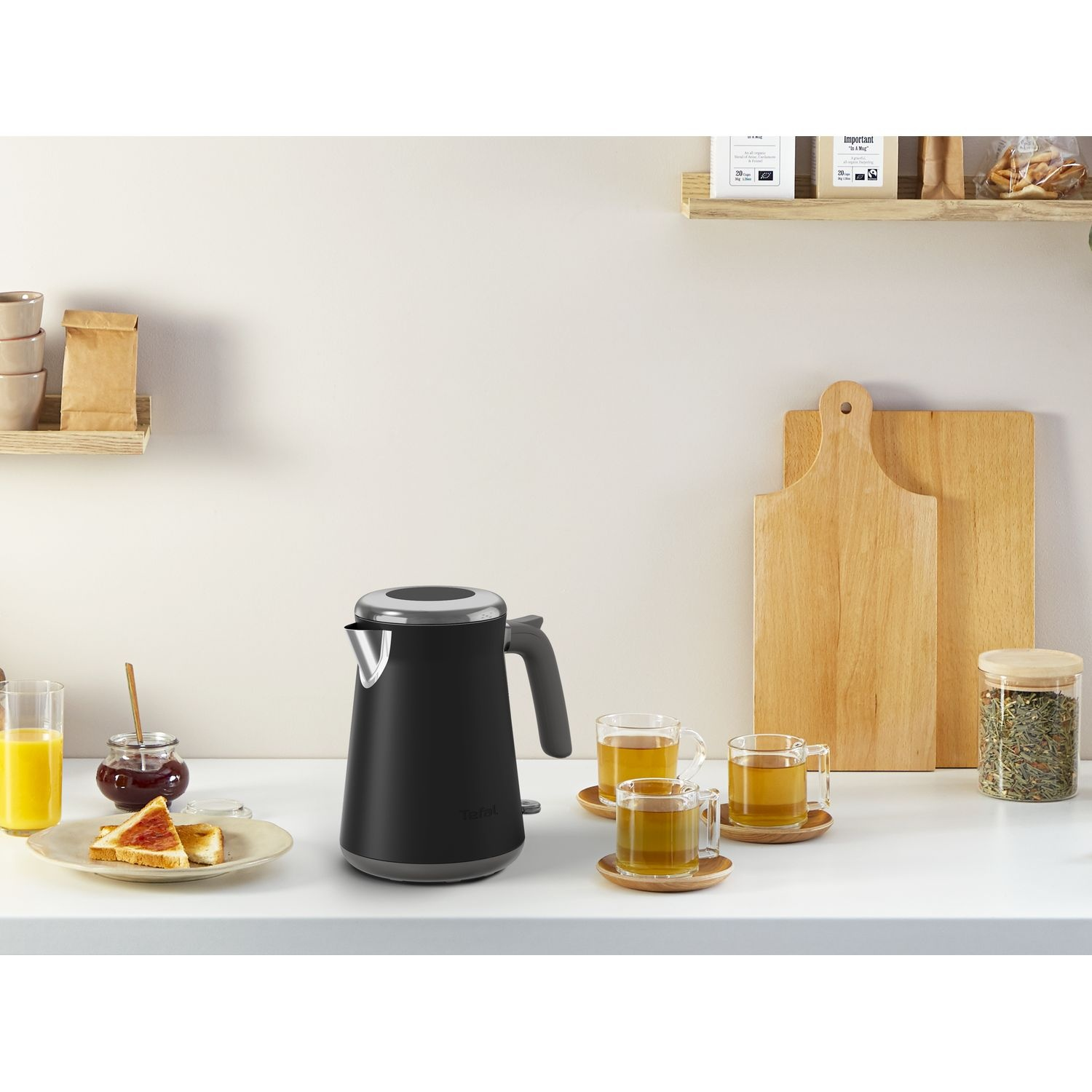A black kettle, two cups of tea, toast, and a glass of juice on a white counter.