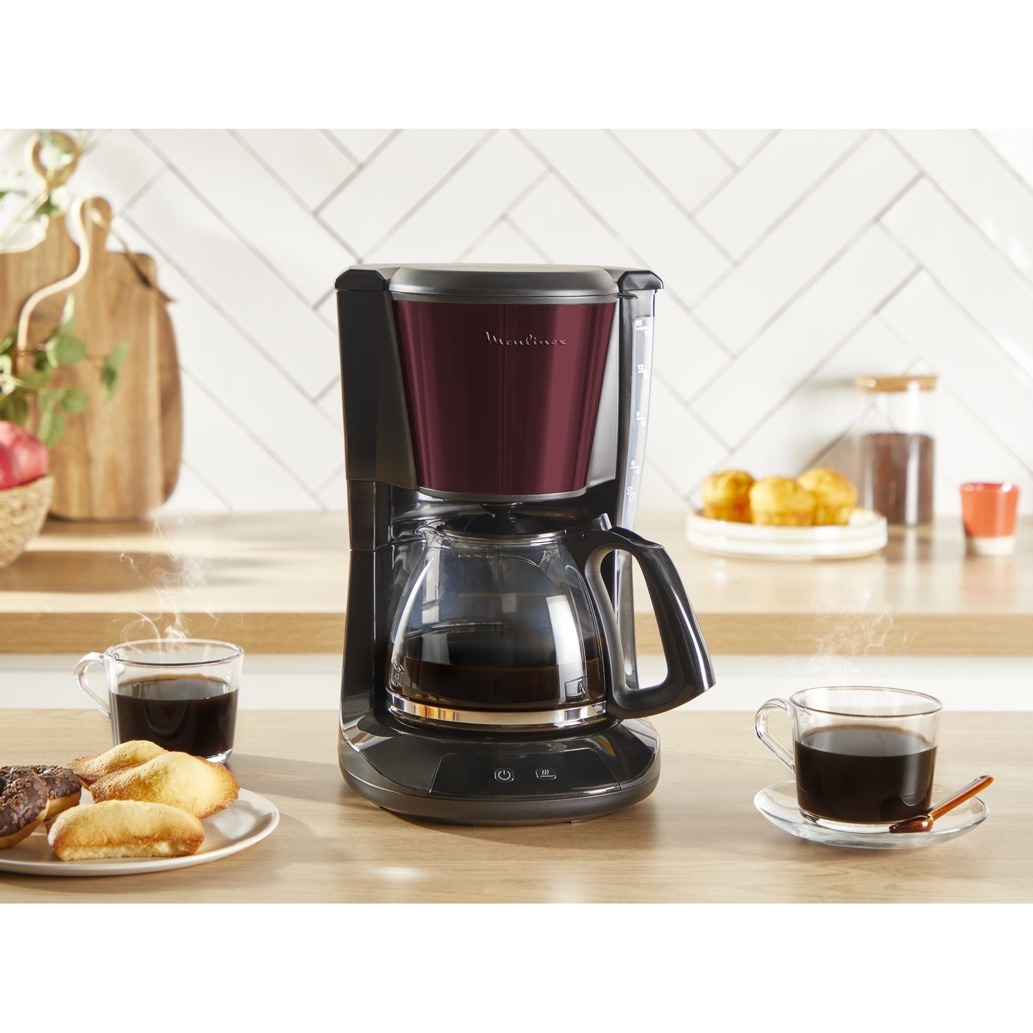 Coffee maker with a carafe, cups of coffee, pastries, and a wooden background.