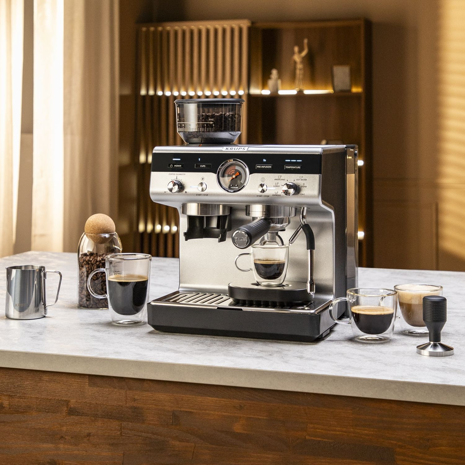 Machine à expresso avec accessoires sur un comptoir. Comprend du café, des verres, un tasseur et une cruche en inox.