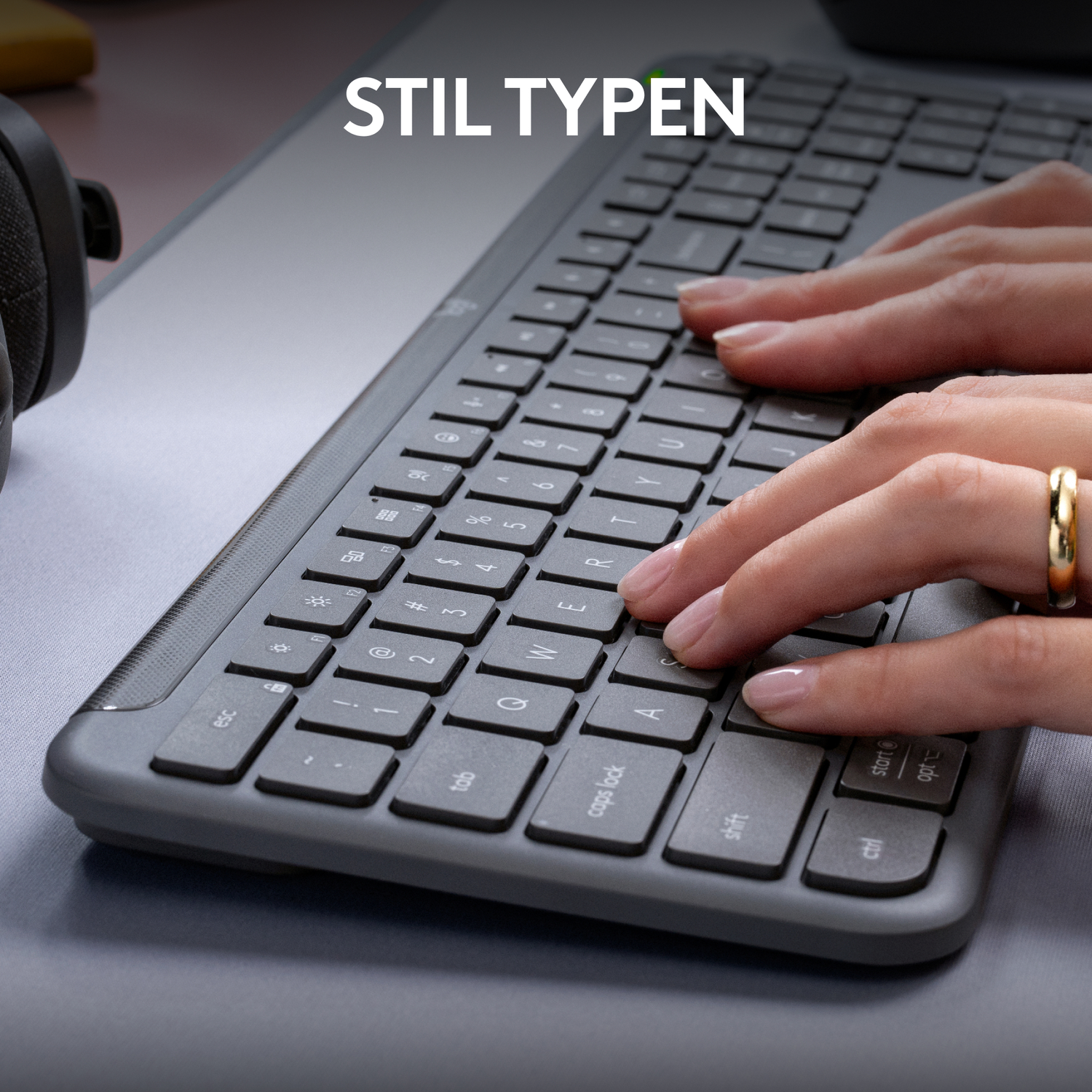 Hands typing on a gray keyboard with a gold ring, close-up shot.