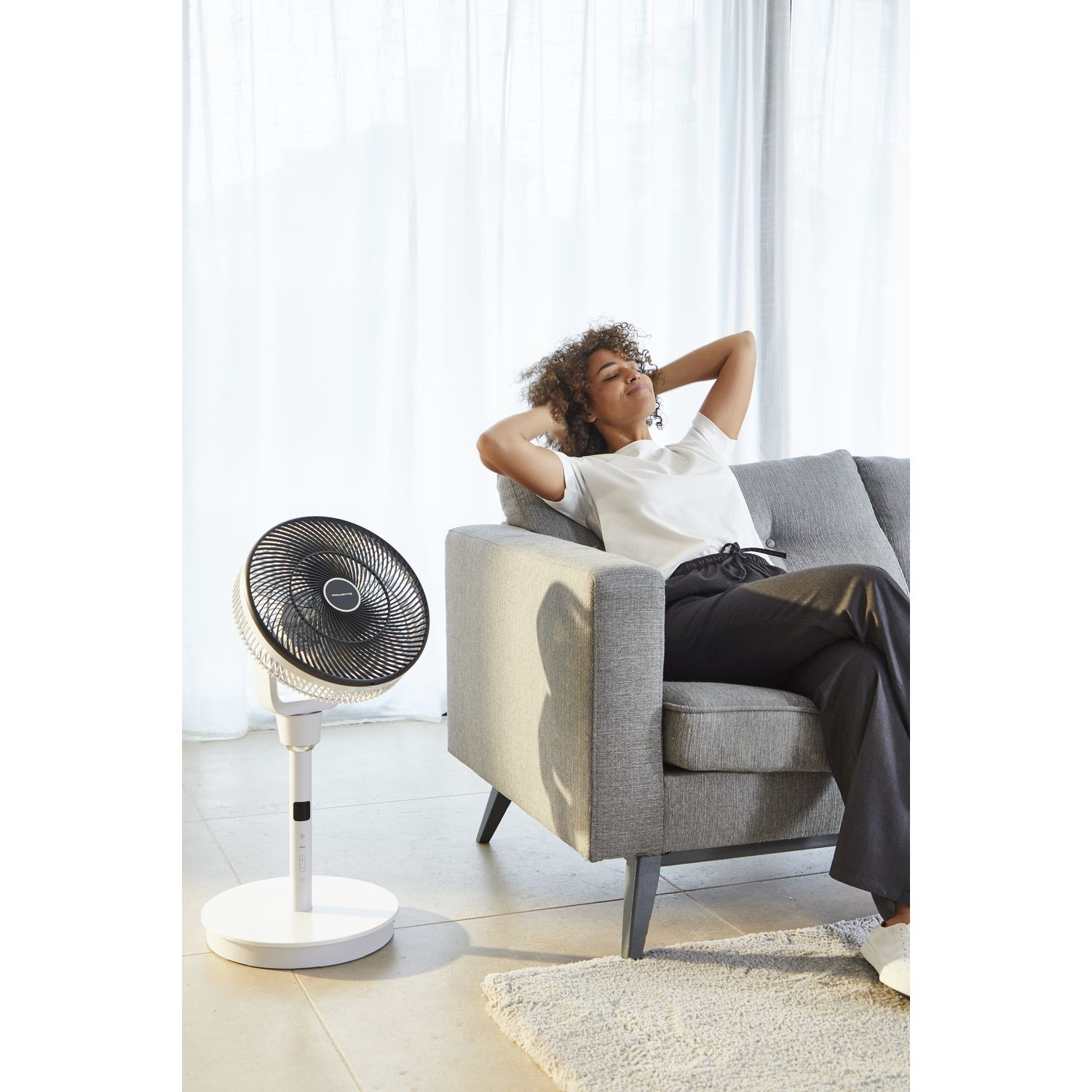 Woman relaxing on a sofa with a standing fan in the living room.