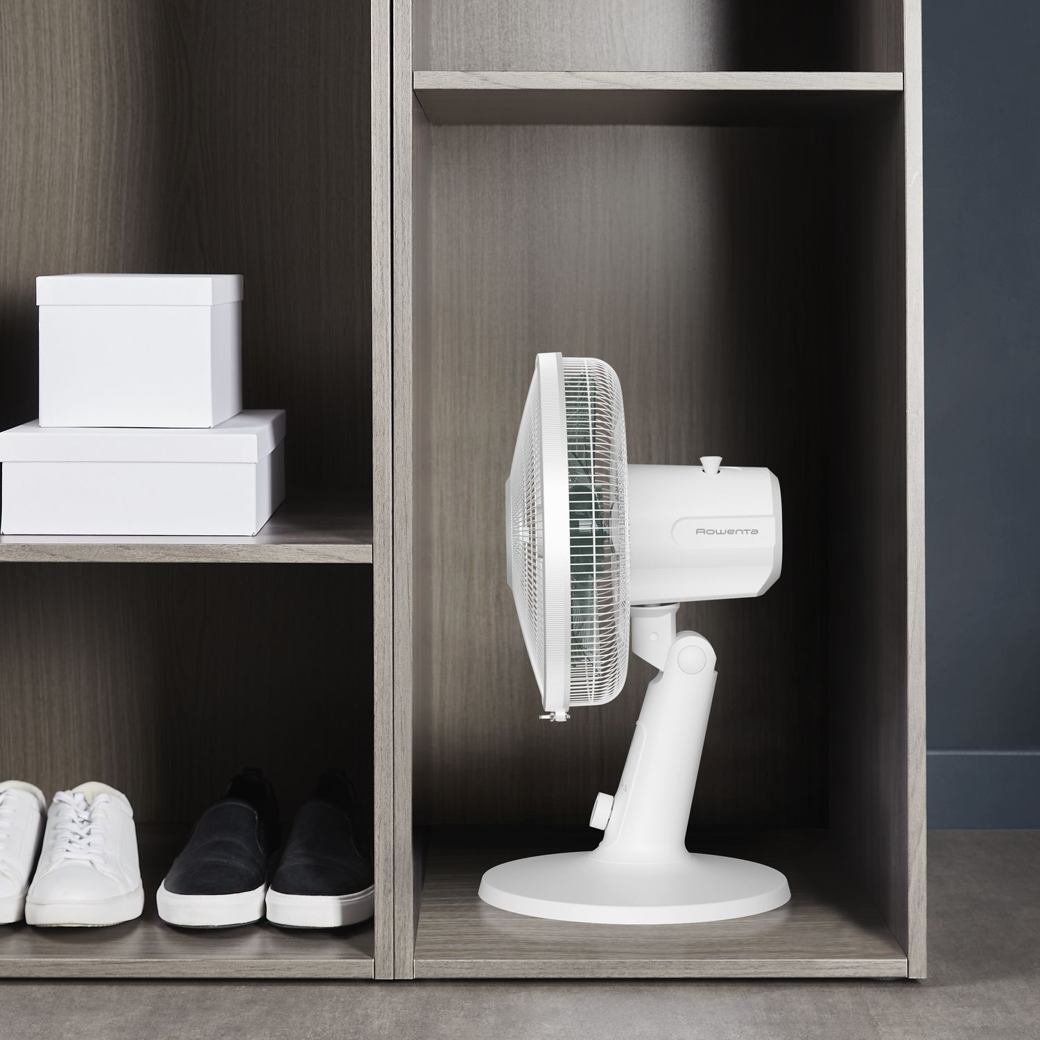 White fan inside a wooden cabinet. Two white boxes are on the shelf above.